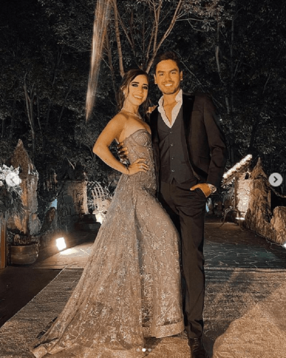 Tammy Parra and Omar Núñez posing elegantly dressed outside a garden