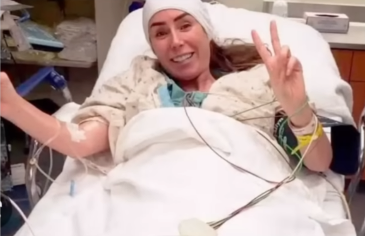 Inés Gómez Mont acostada en una cama de hospital luego de una cirugía en el cerebro sonríe a la cámara y hace la señal de la victoria