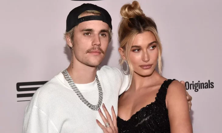 Justin y Hailey Bieber posan abrazados en un evento ella lleva el cabello recogido en un chongo él trae una gorra puesta al revés