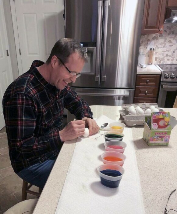 hombre haciendo huevos de pascua en el comedor de su casa 