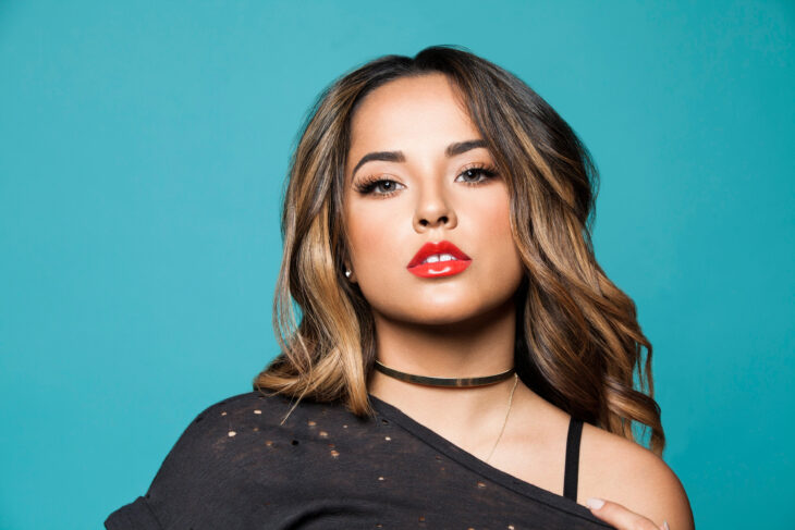 Becky G en actitud sexy lleva labial rojo intenso y maquillaje marcado