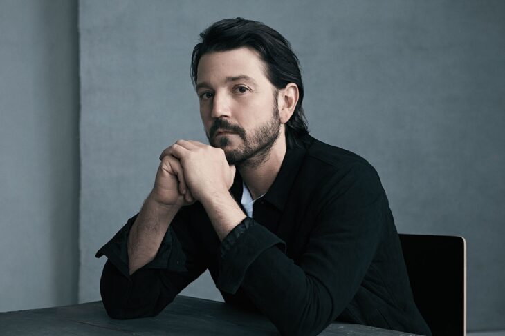 Diego Luna posa pensativo con ambas manos tocandose la barbilla lleva el cabello relamido y una notable barba y bigote