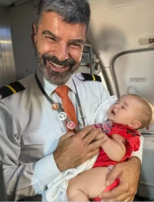 un sobrecargo sostiene en sus brazos a una bebé mientras sonríe a la cámara lleva su uniforme de asistente de vuelo 