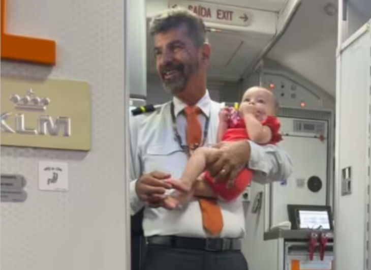 un sobrecargo sostiene a una bebé en brazos mientras esta de pie cerca de la puerta del avión