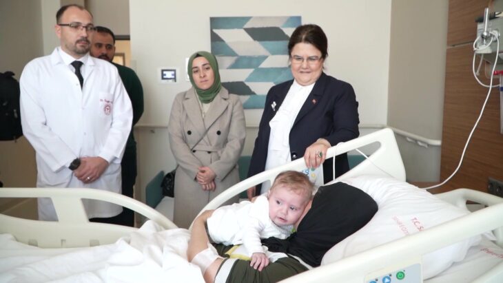 mujer en al cama de un hospital con su bebé en brazos mientras es rodeada por personas del Estado Turco 