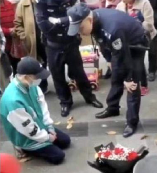 oficiales de la policía dialogan con un hombre que está arrodillado en el pavimento junto con un ramo de flores