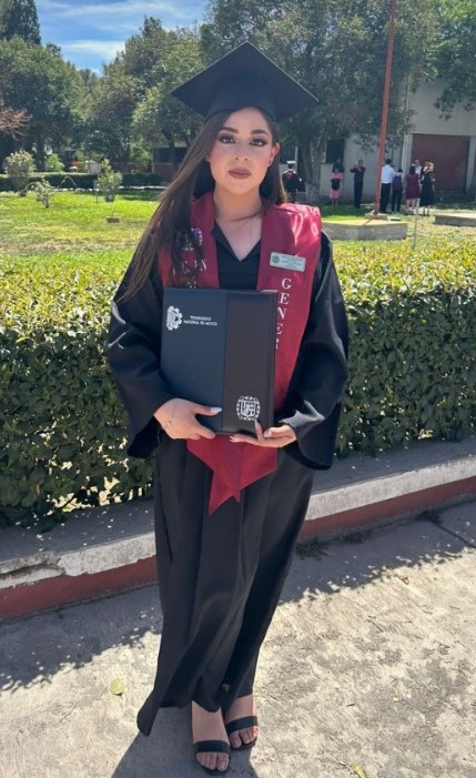 Fotografía de una chica posando con una toga y birrete de graduada frente a un jardín 