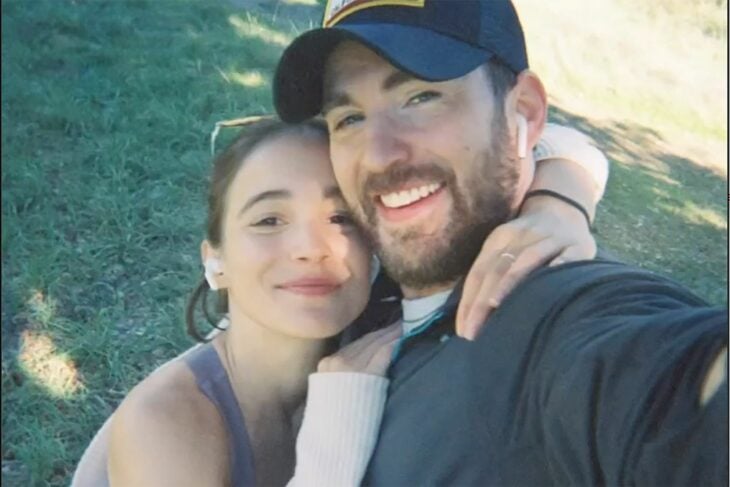 Chris Evans junto a su novia actual la actriz Alba Baptista ambos están posando abrazados para la selfie y llevan ropa deportiva él trae una gorra oscura