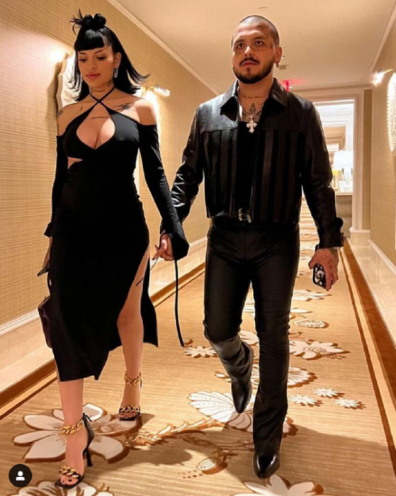 Christian Nodal y Cazzu caminando por el pasillo alfombrado de algún hotel en Las Vegas Nevada EEUU ambos van vestidos de negro