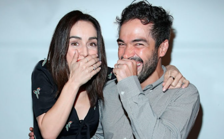 Alfonso Herrera y Ana de la Reguera sonríen divertidos a la cámara mientras se cubren la boca con la mano, como si estuvieran haciendo alguna travesura