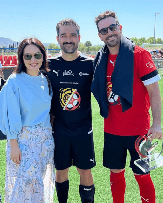 Alfonso Herrera y Ana de la Reguera junto a Mané de la Parra en un evento deportivo ellos llevan uniformes de futbol y Ana ropa casual están en una cancha de futbol