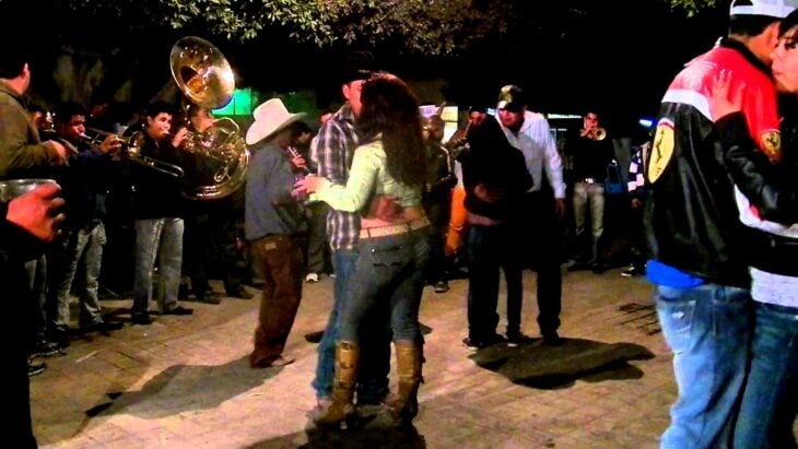 una banda estilo sinaloense tocando en la calle mientras personas bailan