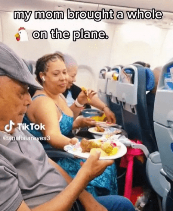 una mujer reparte a un hombre mayor un plato con alimentos en un avión están sentados en la misma fila