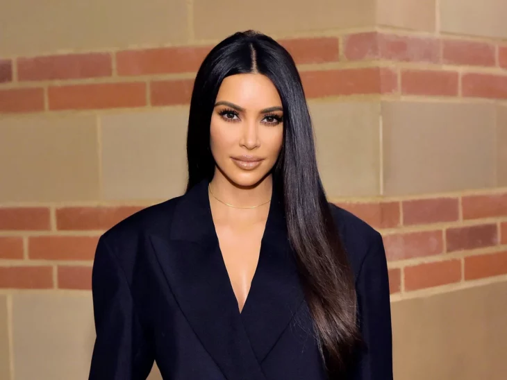 Kim Kardashian en un primer plano posa junto a una pared de ladrillo con vestimenta oscura