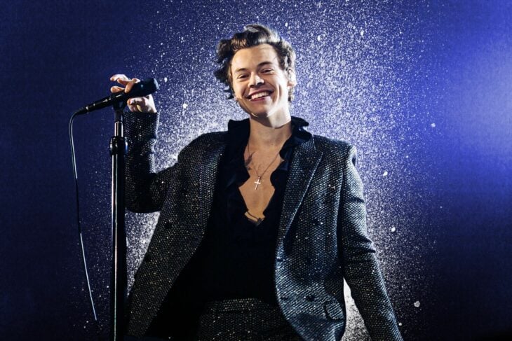 el cantante Harry Styles en el escenario sonríe mientras toma el micrófono que esta en su base con una de sus manos