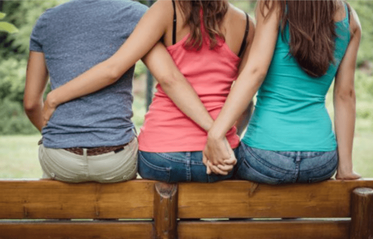 un chico abraza a una chica mientras con su mano sostiene la mano de una segunda chica que está con ellos los tres están de espaldas