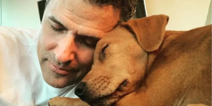 Marco Antonio Regil recargado tiernamente en una de sus mascotas una perrita café