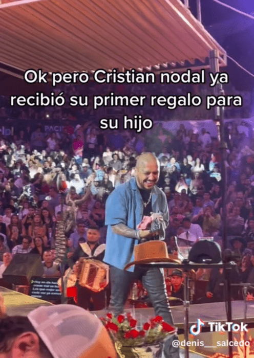 Christian Nodal en el escenario durante un concierto en Tepatitlán Jalisco lleva en las manos ropita de bebé esta rodeado de gente con un look muy relajado