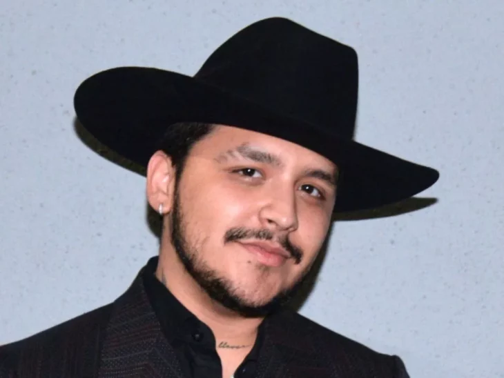 Christian Nodal vestido de negro y está posando con un sombrero también negro puesto