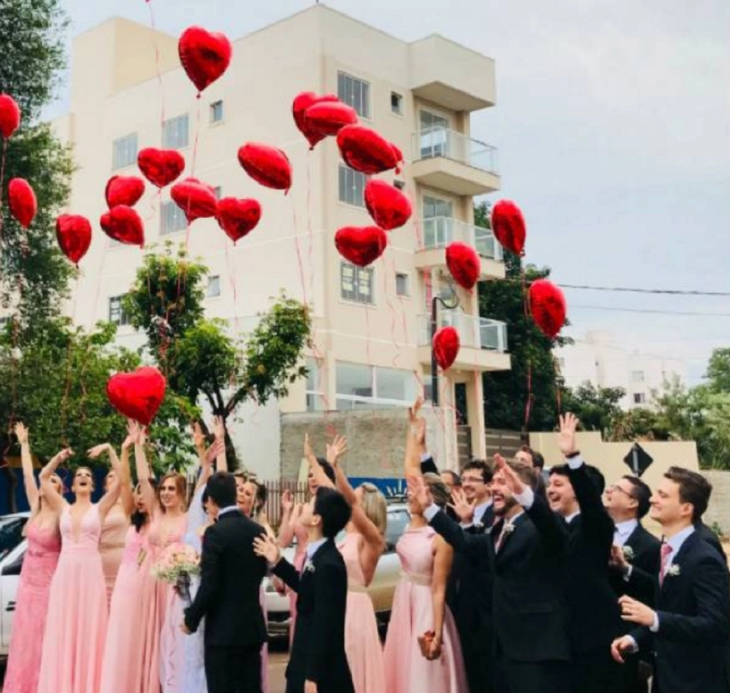 damas y padrinos de honor de una boda sueltan globos de color rojo al cielo
