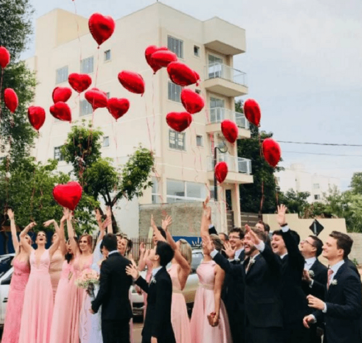 damas y padrinos de honor de una boda sueltan globos de color rojo al cielo