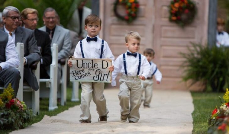 unos pequeños niños caminando al altar para abrirle paso a la novia llevan un cartel en las manos