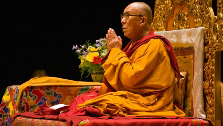 Imagen del Dalai Lama en un evento religioso lleva la vestimenta tradicional de los tibetanos y está juntando sus manos 