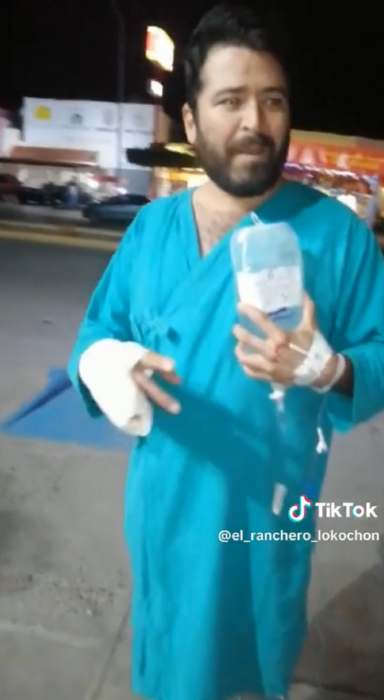 un paciente del IMSS sale a la calle con suero conectado en mano lleva la mano derecha vendada y una bata azul del hospital
