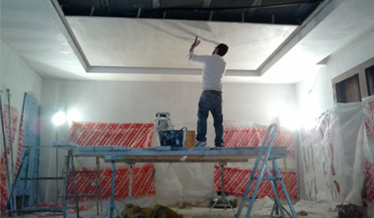 un hombre trabajando en los acabados de yeso en una casa subido en un andamio