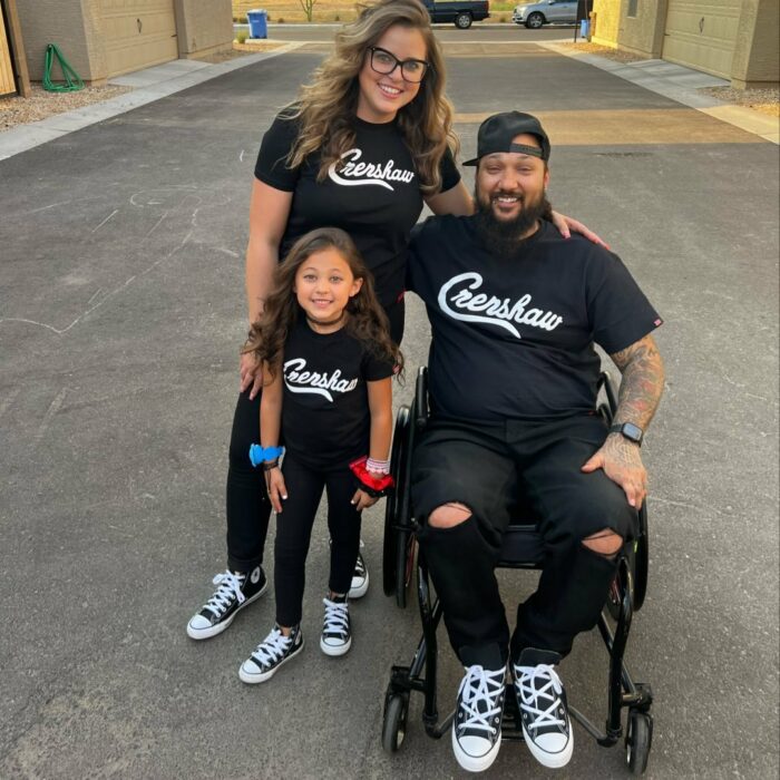 Imagen de una madre y un padre abrazados al lado de su hija de seis años vestidos con una camisa color negro igual 