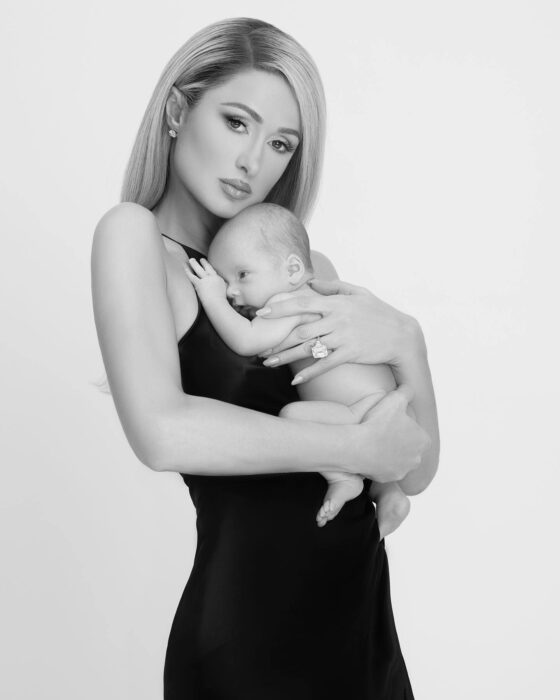 Paris Hilton usando un vestido negro cargando a su bebé sobre su pecho