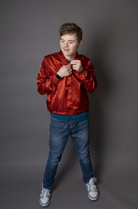 Noah Matthews el joven actor con síndrome de Down posa con una chamarra brillosa de color rojo y jeans