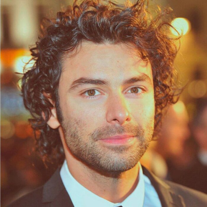 Aidan Turner con traje y cabello largo 