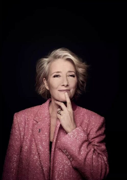 Emma Thompson con traje rosa y fondo negro 