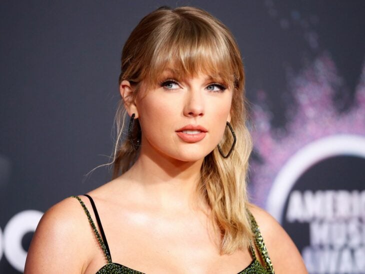 Taylor Swift posando en un evento de música está mirando a un punto diferente de la cámara lleva un vestido de tirantes