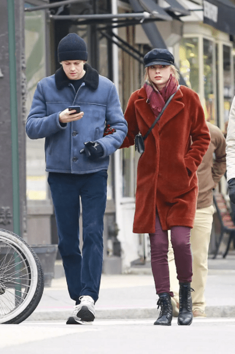 Taylor Swift and Joe Alwyn walk through the streets she takes his arm they are both wearing winter clothes