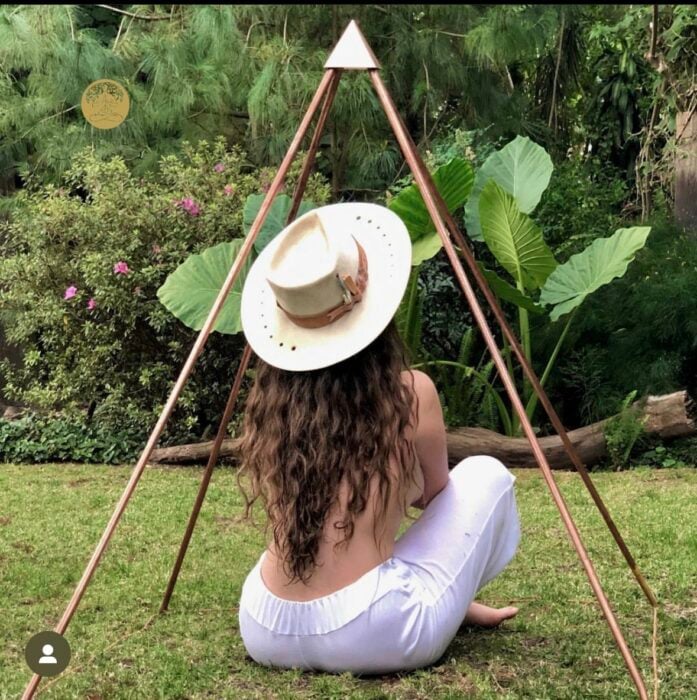 mujer con sombrero sentada dentro de una pirámide de cobre en un jardín 