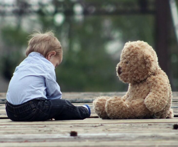 Niño sentado en el suelo con su oso de peluche frente a él