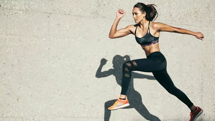 una chica corriendo con ropa deportiva en color negro su sombra se refleja en la pared