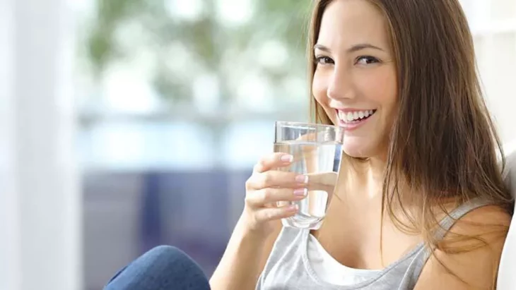 una chica sonríe mientras se lleva a la boca un vaso con agua