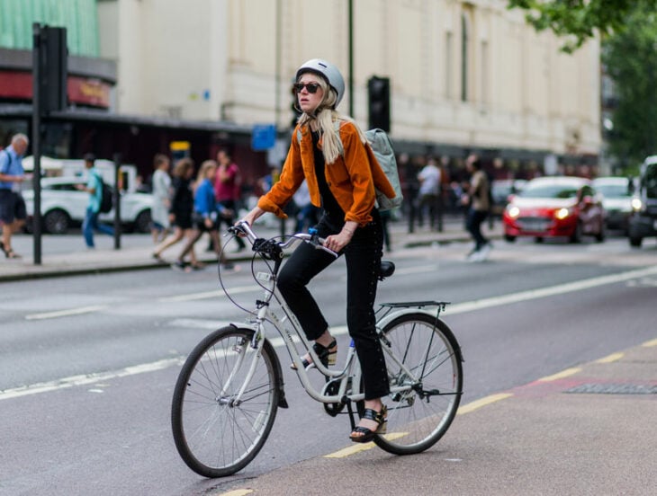 una chica conduciendo por la ciudad en bicicleta lleva en la cabeza un casco protector
