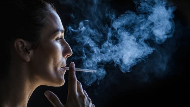 una mujer fumando en la oscuridad se aprecia el humo del cigarro