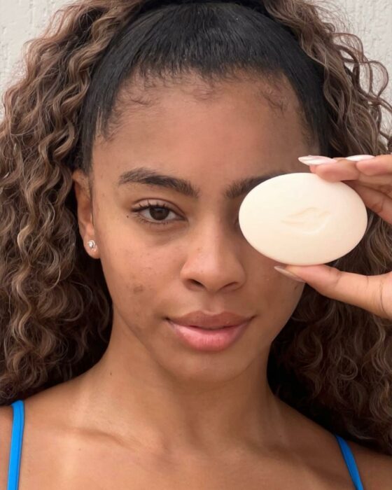 Chica con una barra de jabón Dove en su ojo izquierdo 