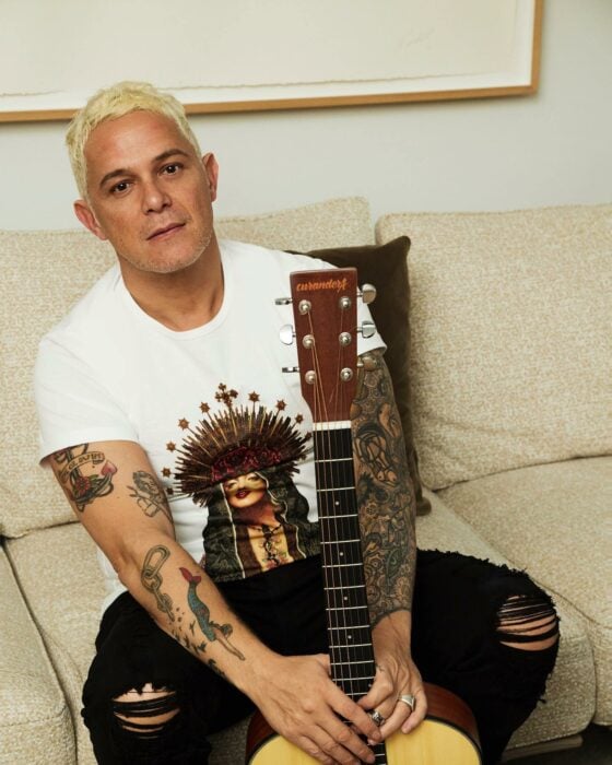 Alejandro Sanz sentado en un sofá con una guitarra entre sus piernas 