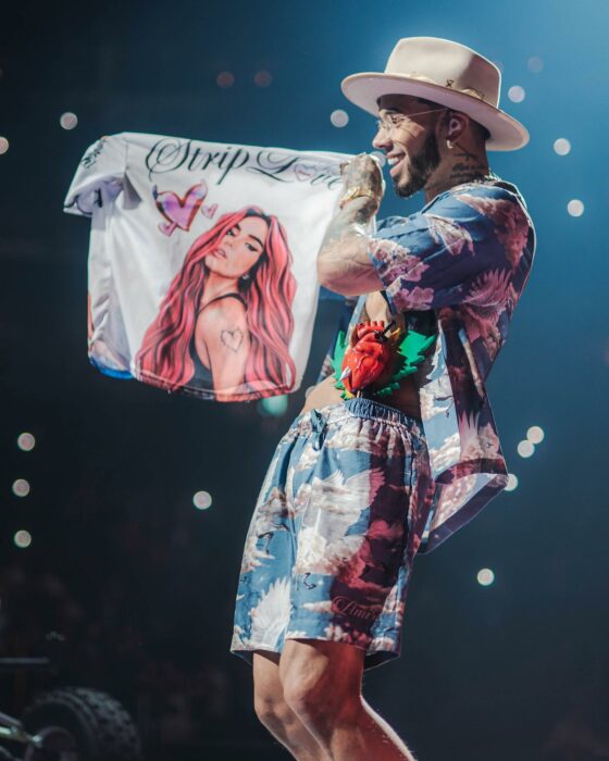 Anuel AA en el escenario de un concierto mostrando una camisa con la cara de Karol G 