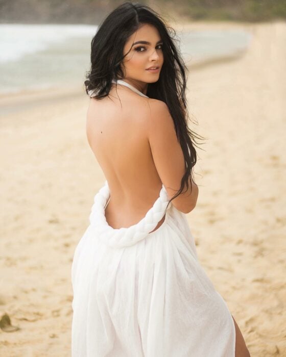 Fotografía de una modelo posando en una playa con un vestido blanco con la espalda descubierta