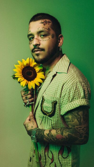 Christian Nodal posando en un fondo verde con un girasol en la mano 