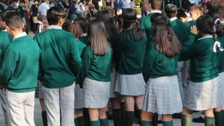 Fotografía que muestra a estudiantes de una escuela usando uniformes de espaldas 