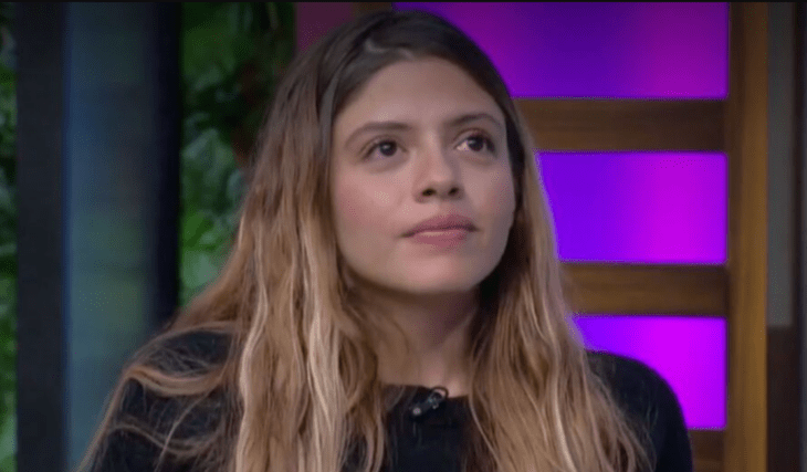 Daniela Parra en un foro de televisión con luces de colores lleva el cabello suelto y largo