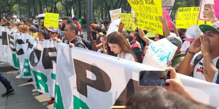 personas caminan con una manta al frente en una manifestación por las calles